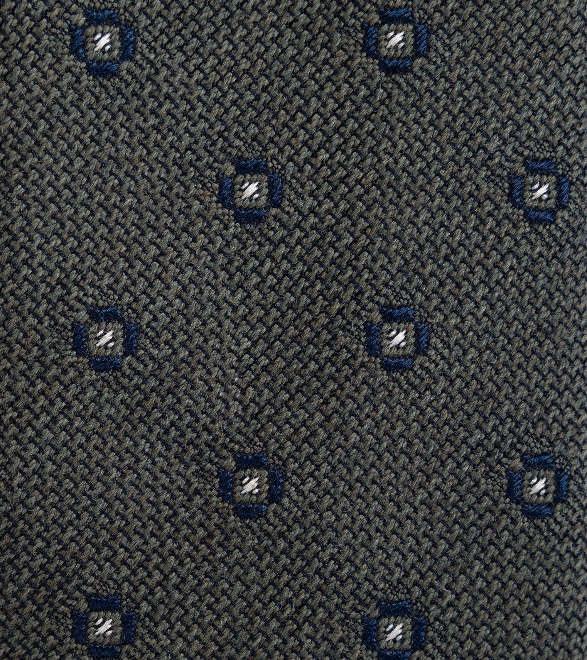 Close-up of a woven necktie fabric in dark gray, featuring a repeating pattern of small blue geometric medallions with white center details.