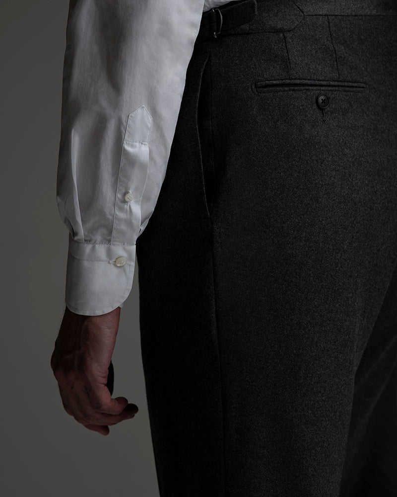 Close-up of a person wearing a light gray shirt and dark gray pants on a gray background