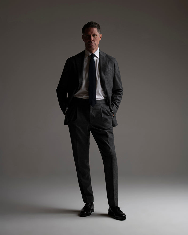 Man wearing a dark grey flannel suit and tie against a grey background