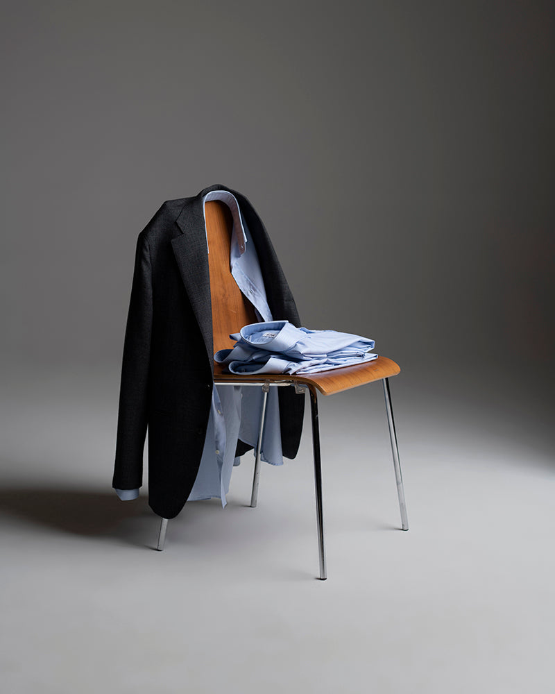 Black jacket draped over a chair with folded clothes underneath on a gray background