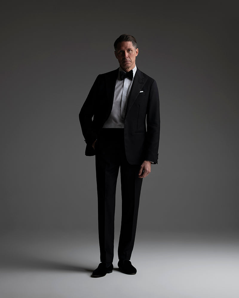 Man wearing a black tuxedo against a gray background
