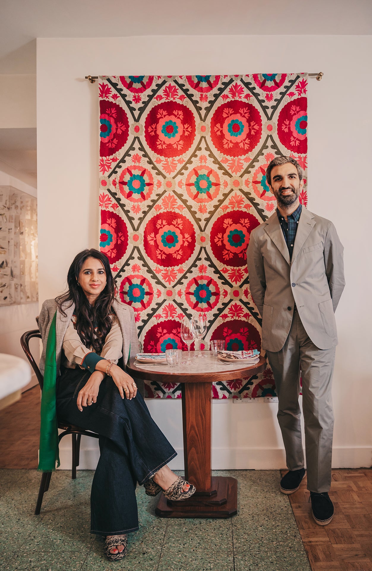 Two people standing in a room with a decorative tapestry on the wall.