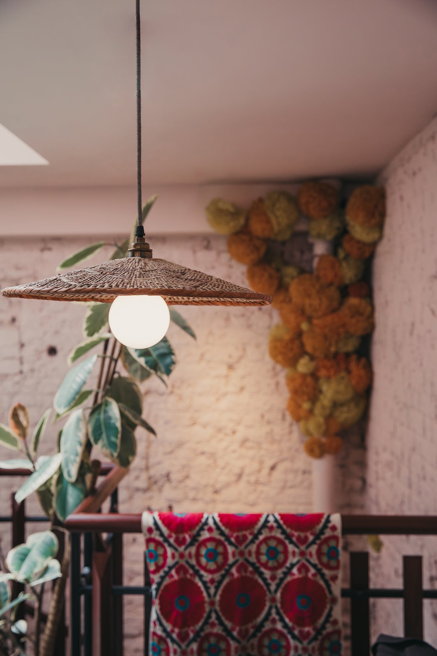 Woven pendant light fixture hanging above a table with a colorful tablecloth.