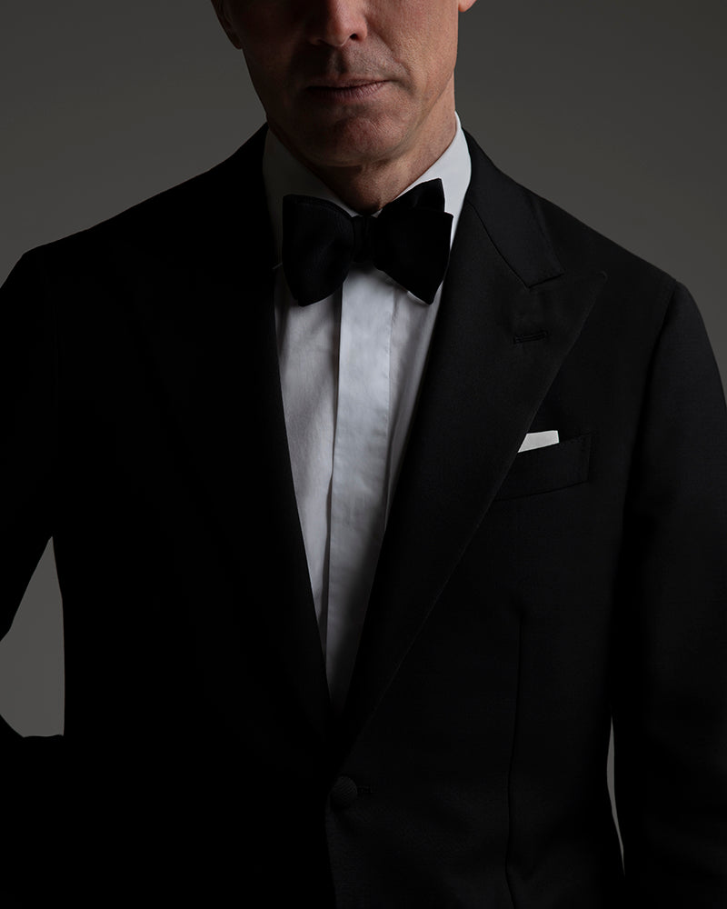 Man wearing a black tuxedo with a bow tie on a dark background