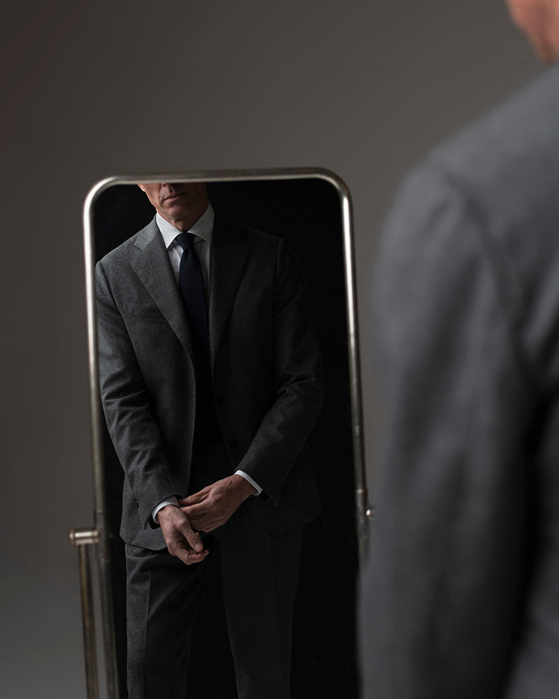 Man adjusting his suit in front of a mirror with a dark background